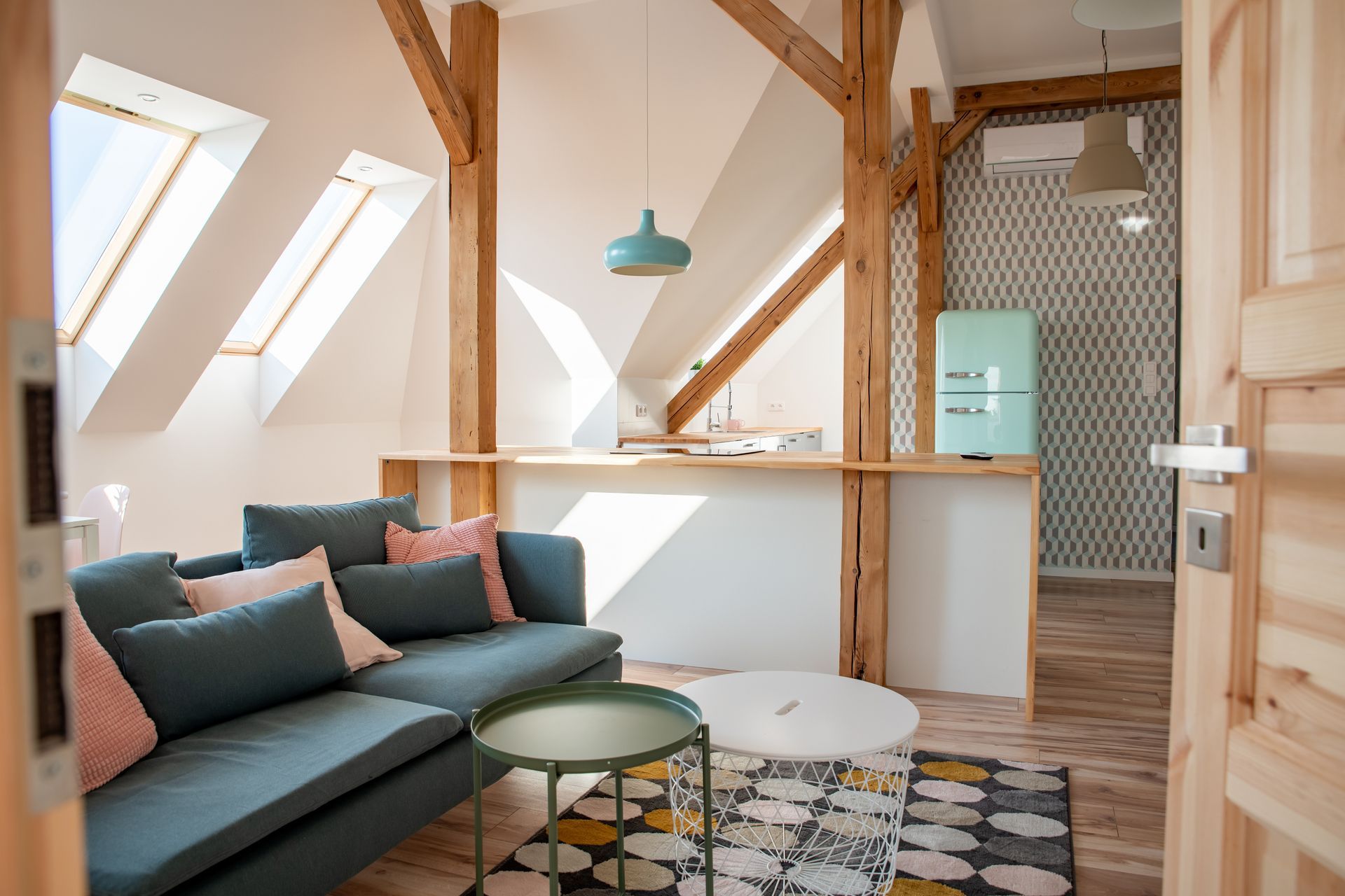 Loft confortable avec canapé bleu, poutres en bois, réfrigérateur pastel et tapis.