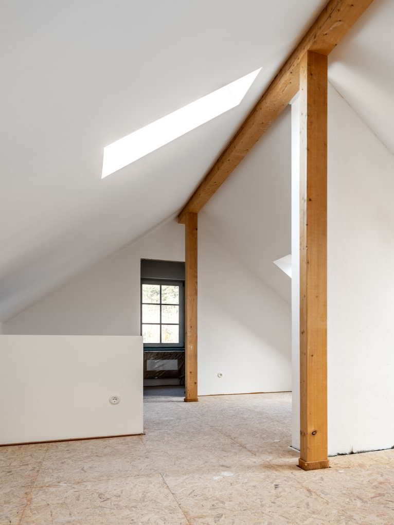 Chambre mansardée avec murs blancs, poutres en bois et petite fenêtre.