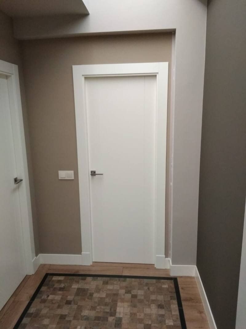 Un pasillo con una puerta blanca y una alfombra en el suelo.