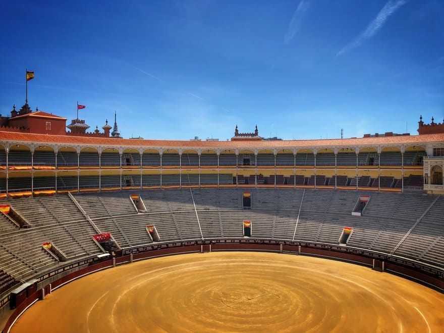 Una plaza de toros vacía con un cielo azul al fondo.