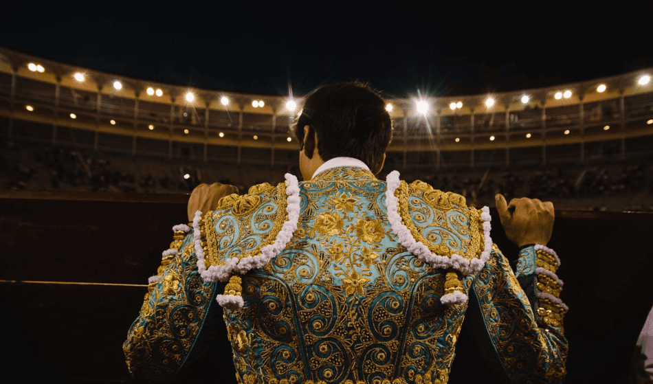 Un hombre vestido de matador está parado en un estadio por la noche.