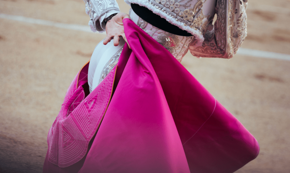 Un matador lleva una capa rosa y una chaqueta blanca.