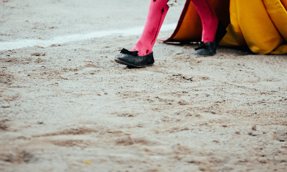Una persona que lleva medias rosas y zapatos negros está parada en un campo de tierra.