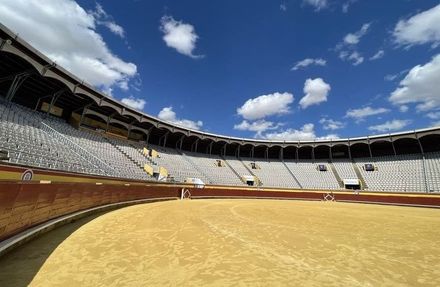Una plaza de toros vacía con un cielo azul y nubes al fondo.