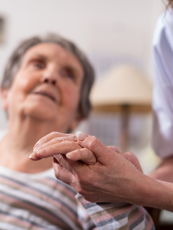 Une personne âgée tient la main d'une soignante.