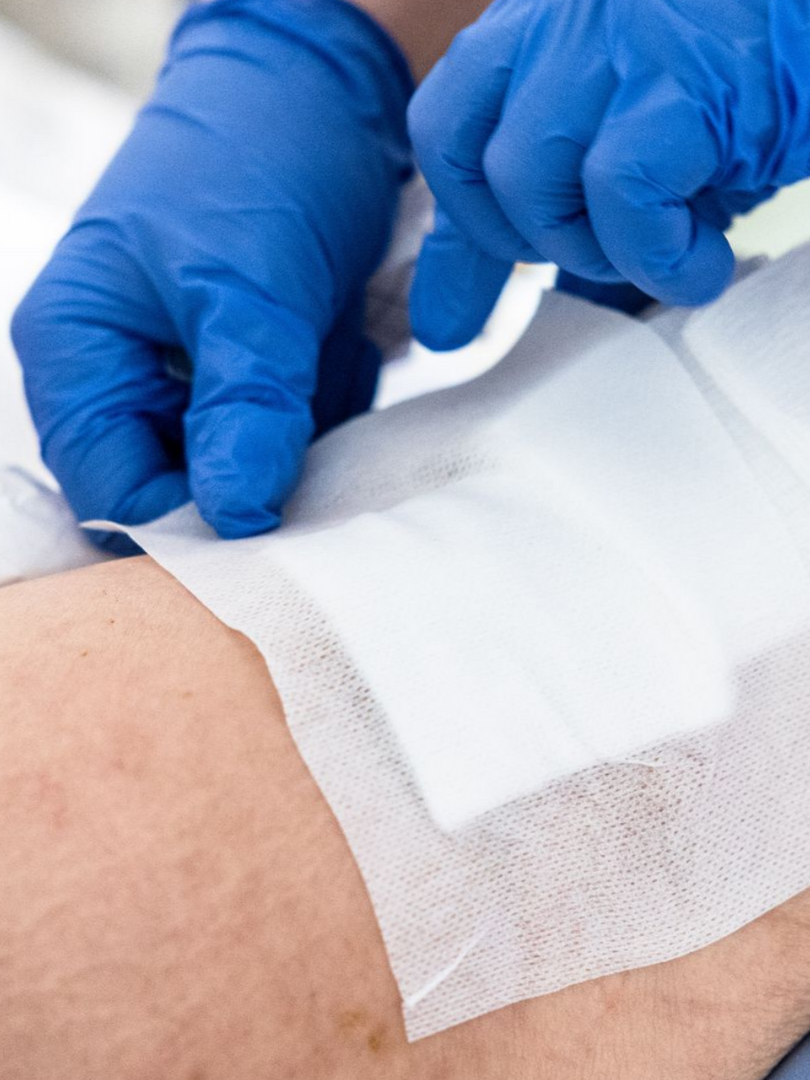 Des mains gantées appliquent un bandage de gaze sur une jambe.