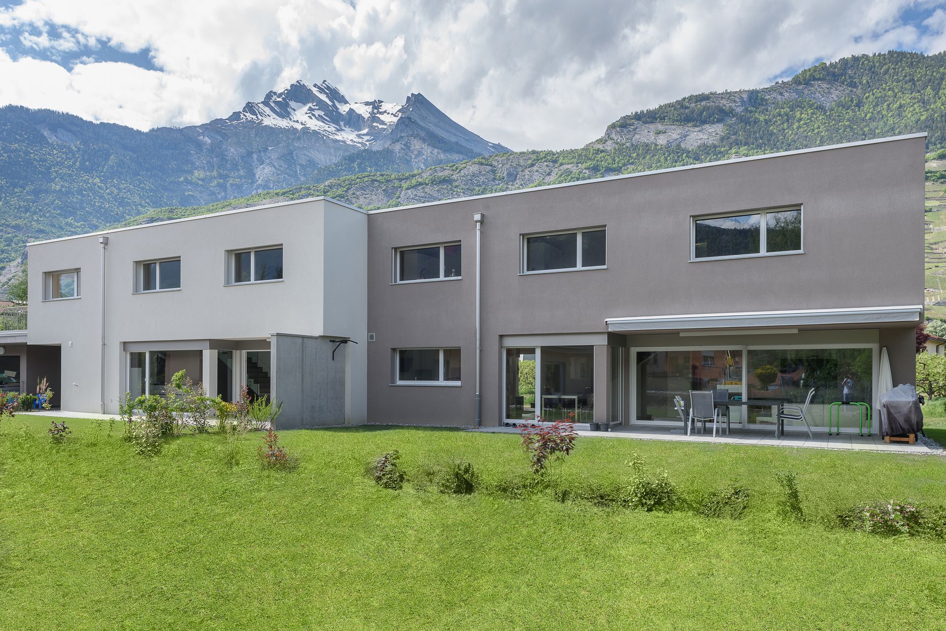 Bâtiment moderne de deux étages avec pelouse verte et montagnes en arrière-plan.