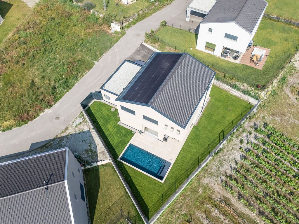 Vue aérienne d'une maison moderne avec piscine, panneaux solaires et jardin gazonné, entourée d'une clôture.
