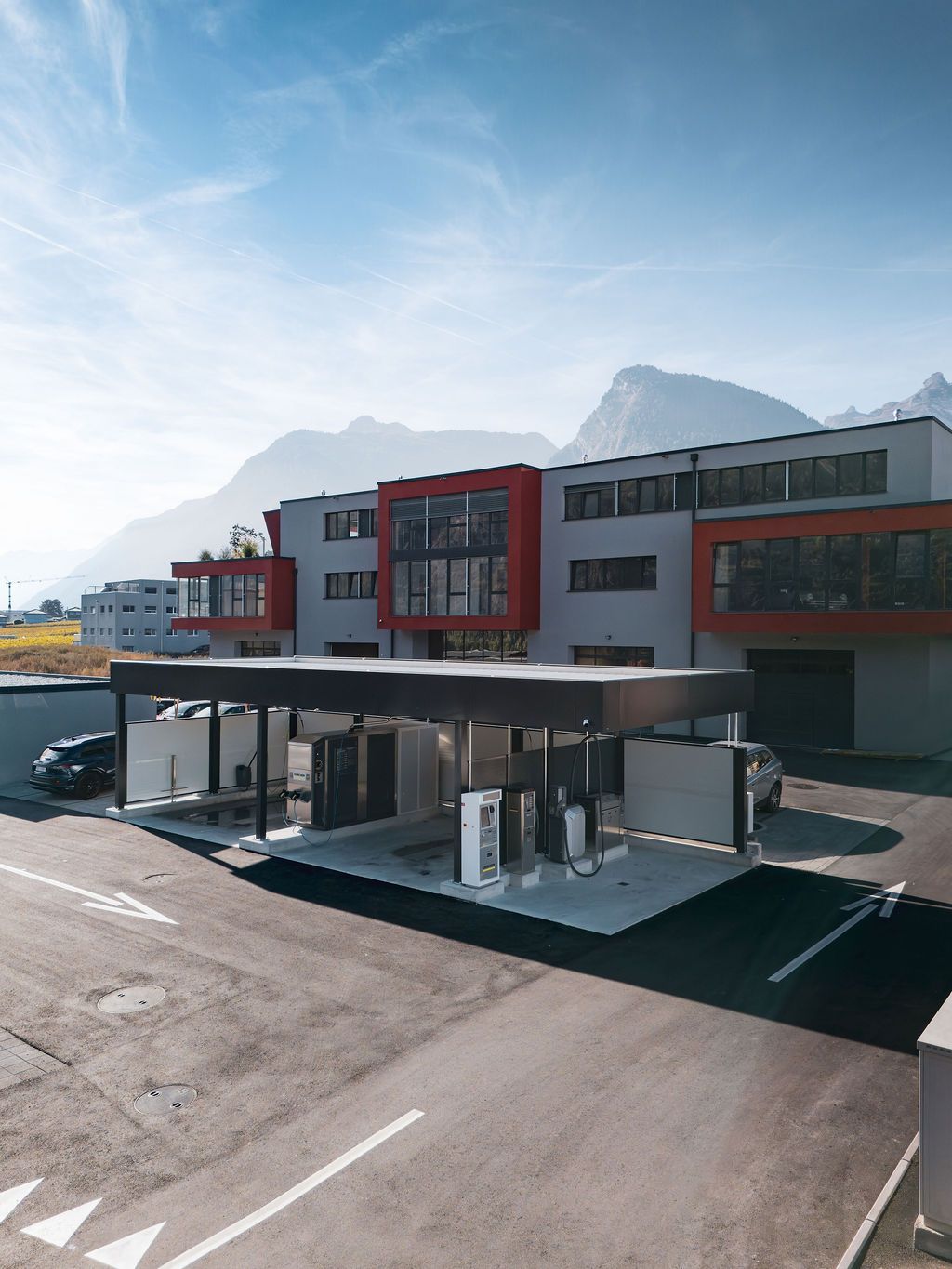 Bâtiment moderne avec des touches de rouge, structure de type abri de voiture et montagnes en arrière-plan.