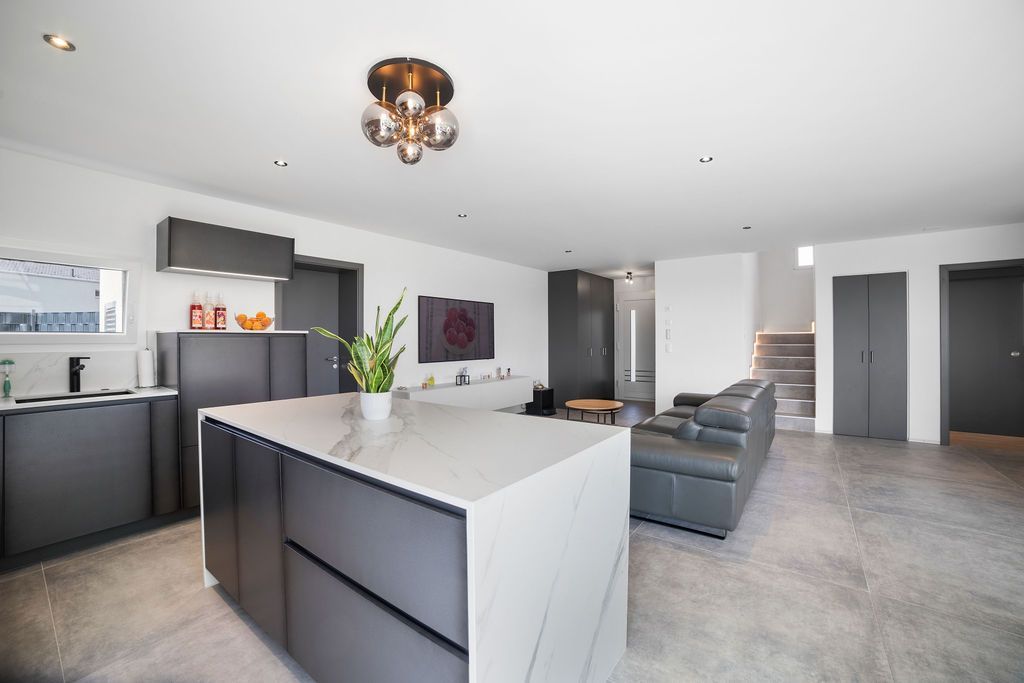 Cuisine et salon modernes à aire ouverte avec armoires grises, îlot en marbre et canapé en cuir.