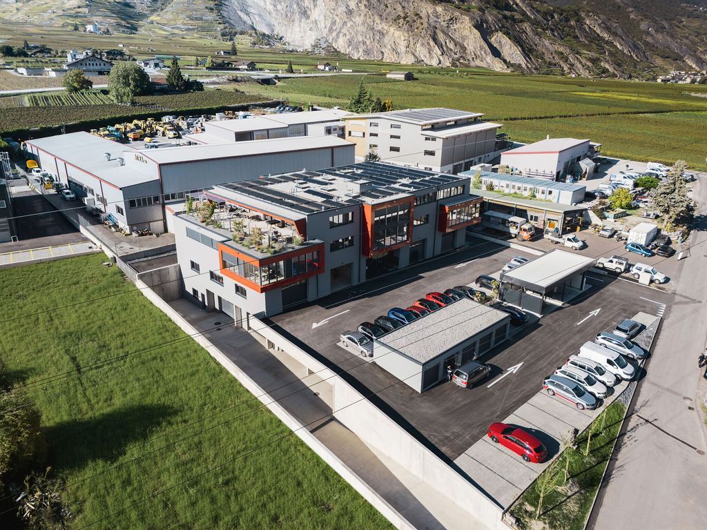 Vue aérienne d'un complexe industriel moderne comprenant plusieurs bâtiments, un parking et une montagne en arrière-plan.