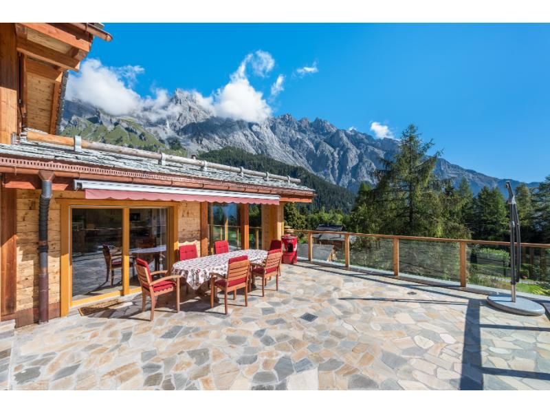 Il y a une table et des chaises sur le balcon d'une maison avec des montagnes en arrière-plan.