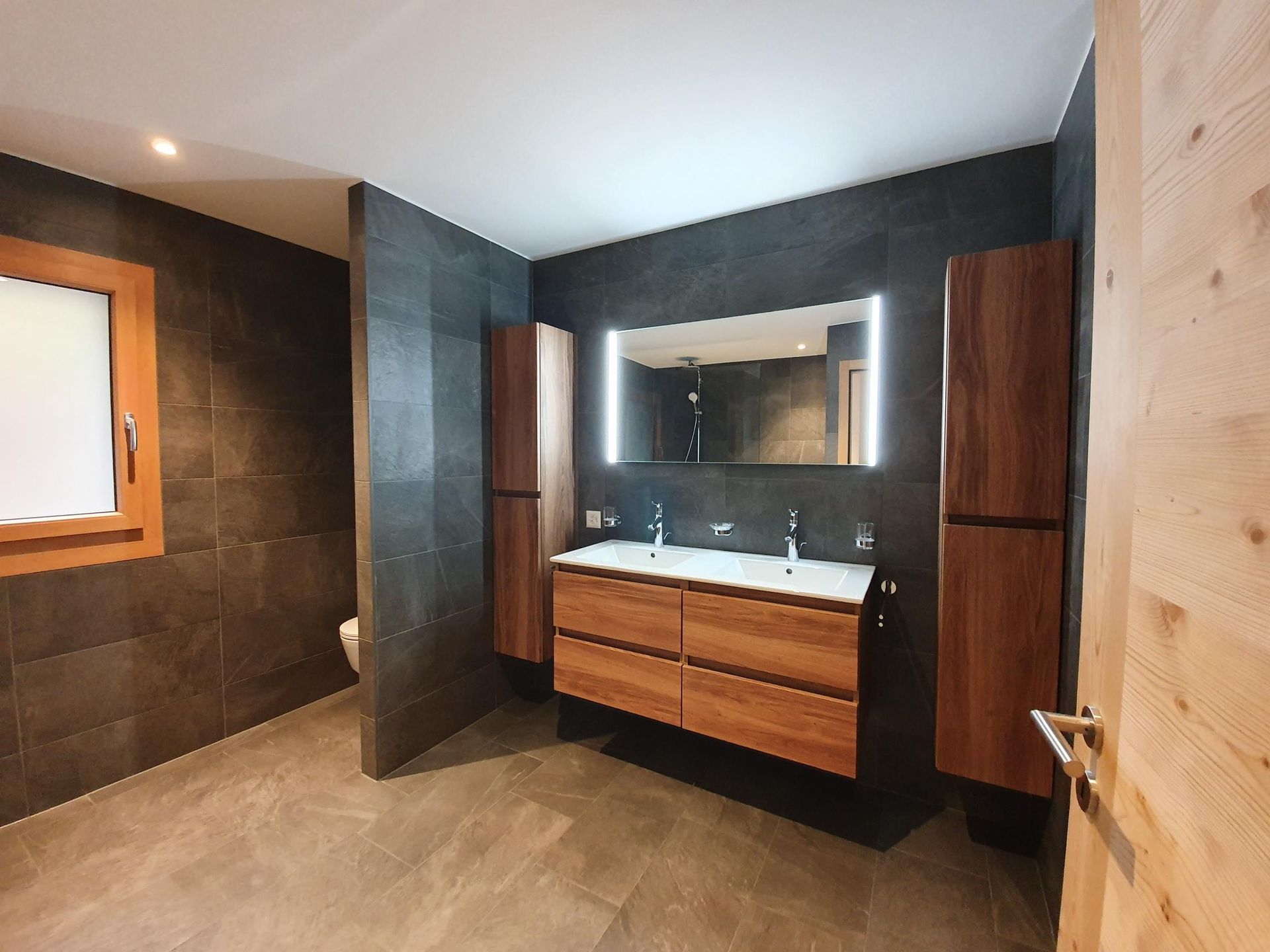 Une salle de bain avec deux lavabos, un WC et un miroir.