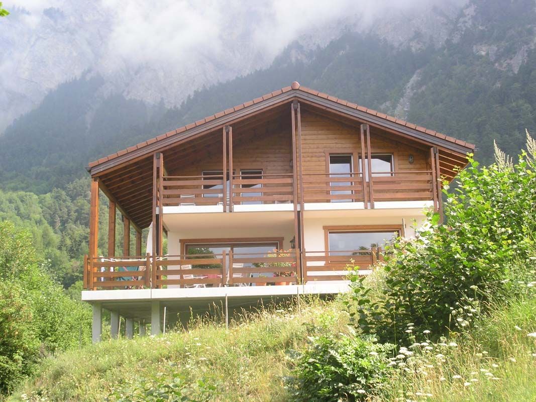 Une grande maison en bois avec un balcon et des montagnes en arrière-plan.