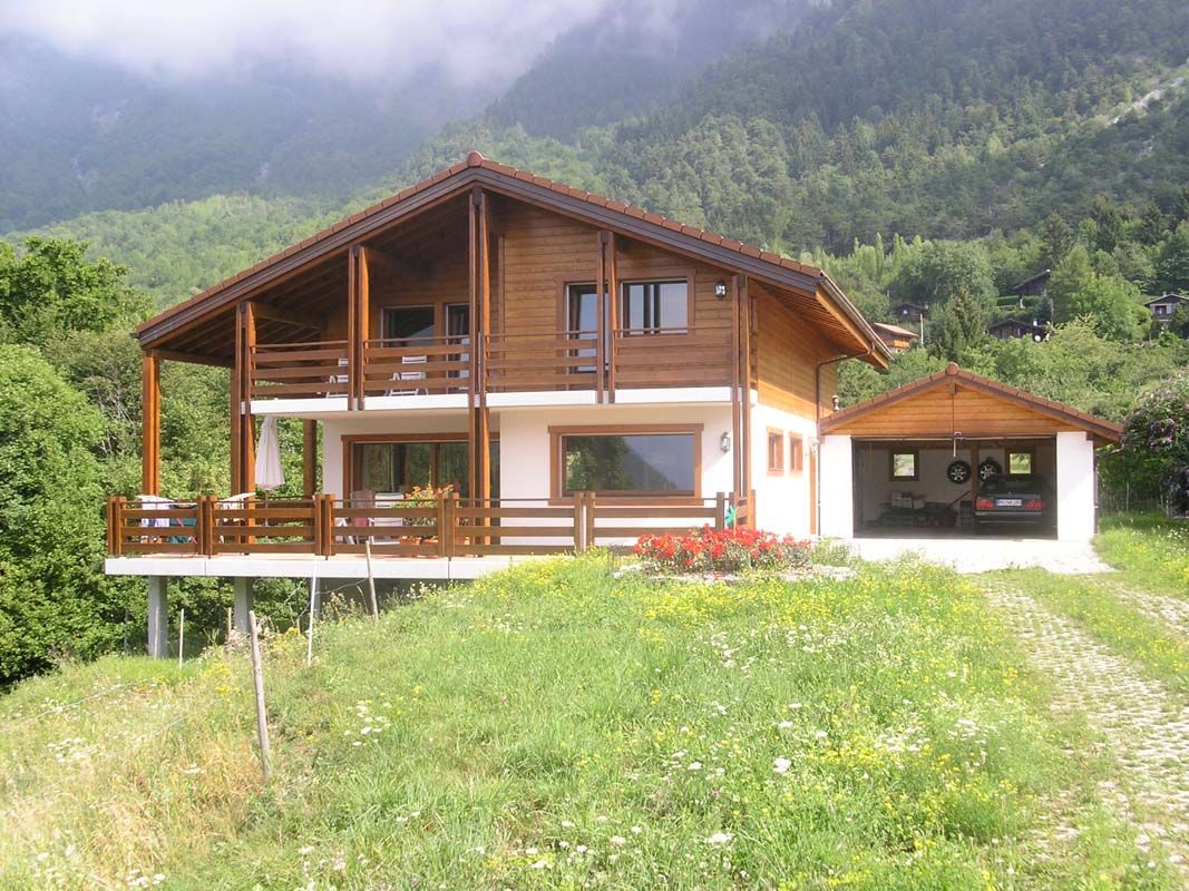 Une grande maison en bois est assise au sommet d'une colline herbeuse.