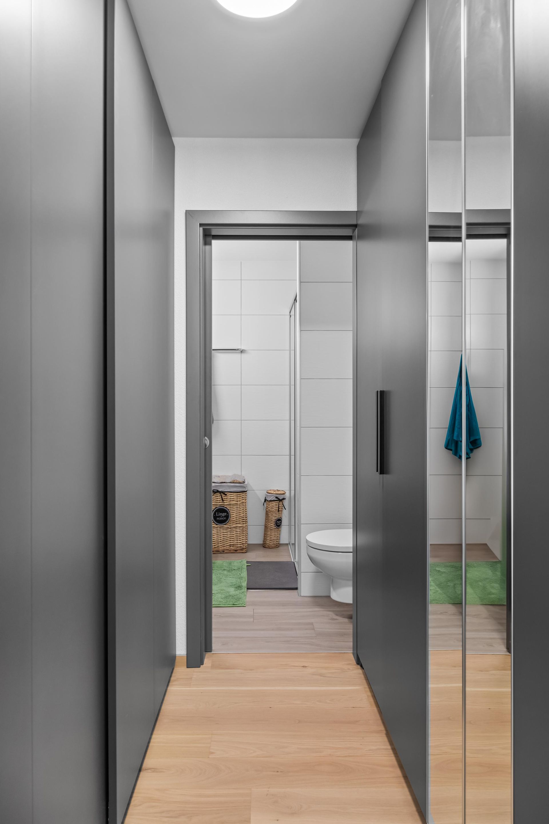 Un couloir menant à une salle de bain avec WC et miroir.