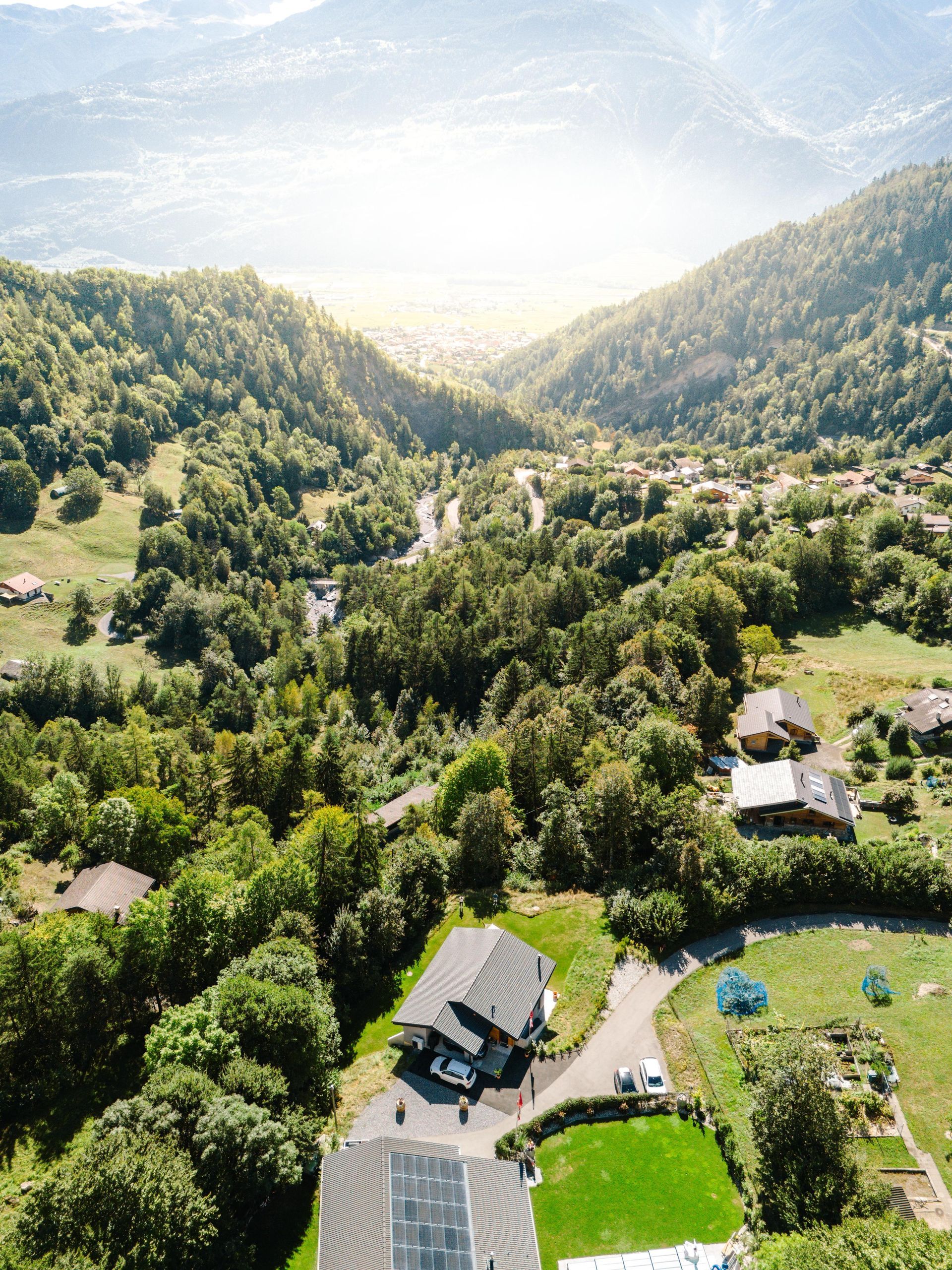 Une vue aérienne d'une maison au milieu d'une vallée entourée d'arbres.