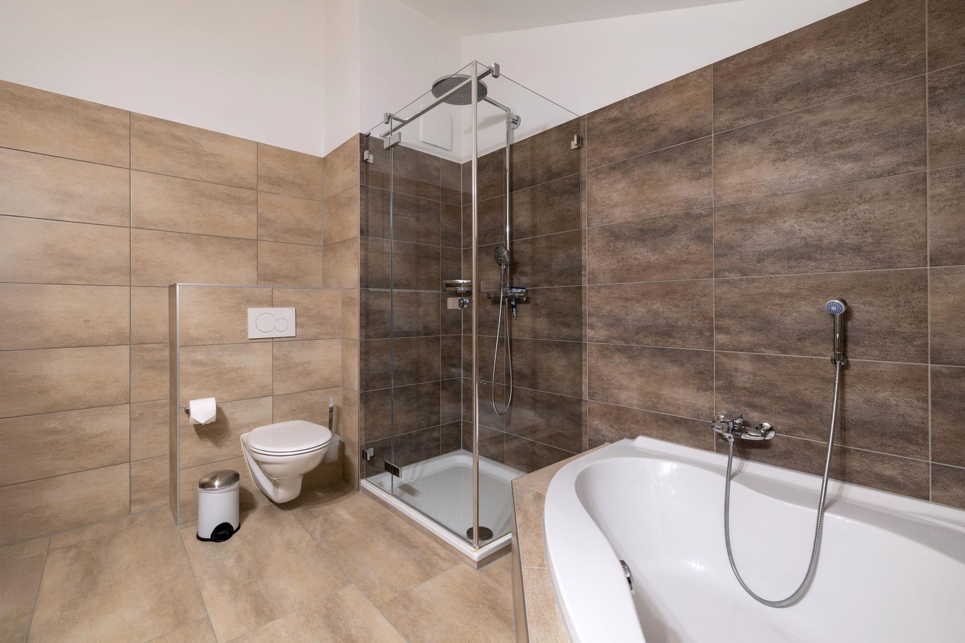 Une salle de bain avec baignoire, douche, toilettes et poubelle.