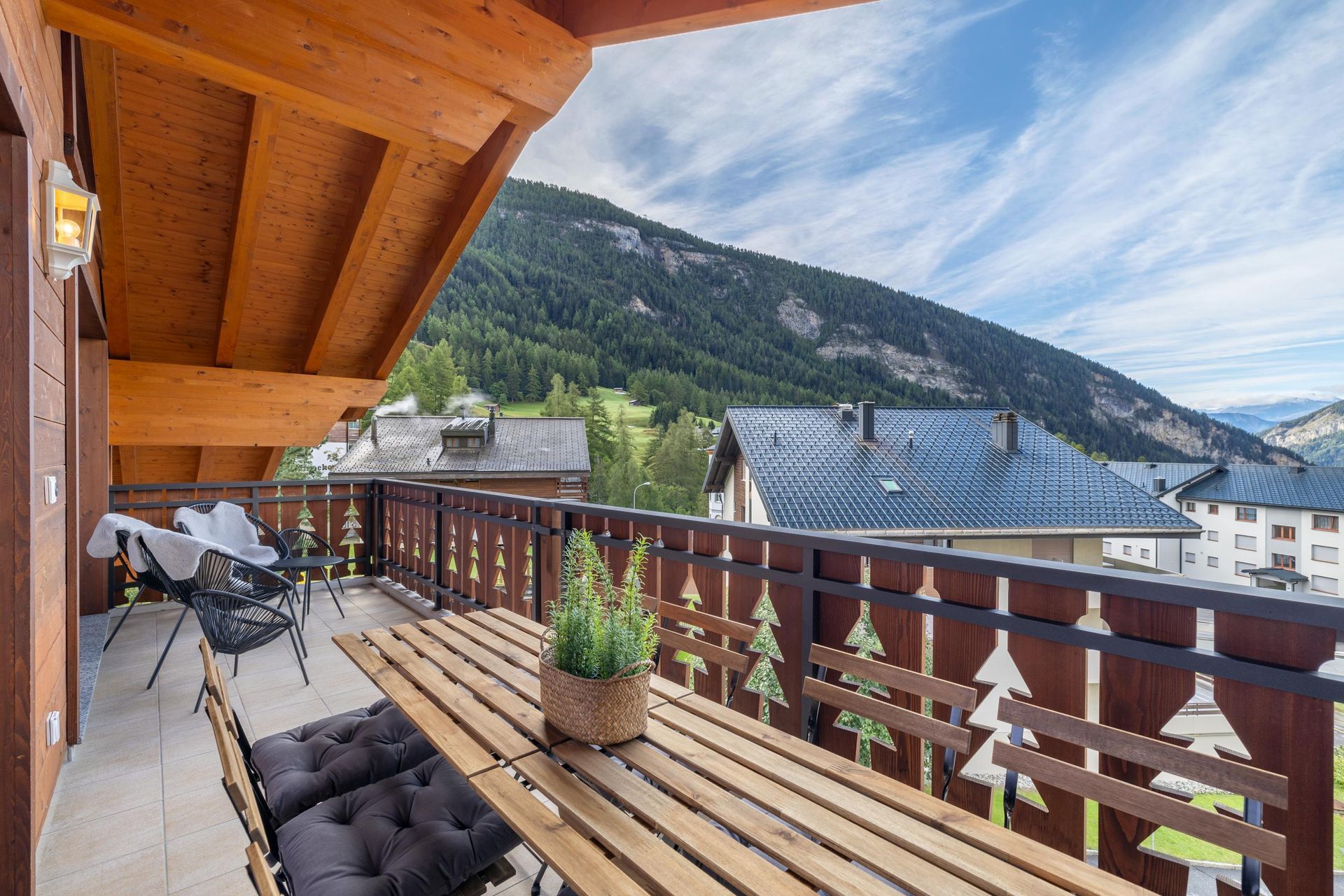 Un balcon avec une table et des chaises en bois et des montagnes en arrière-plan.