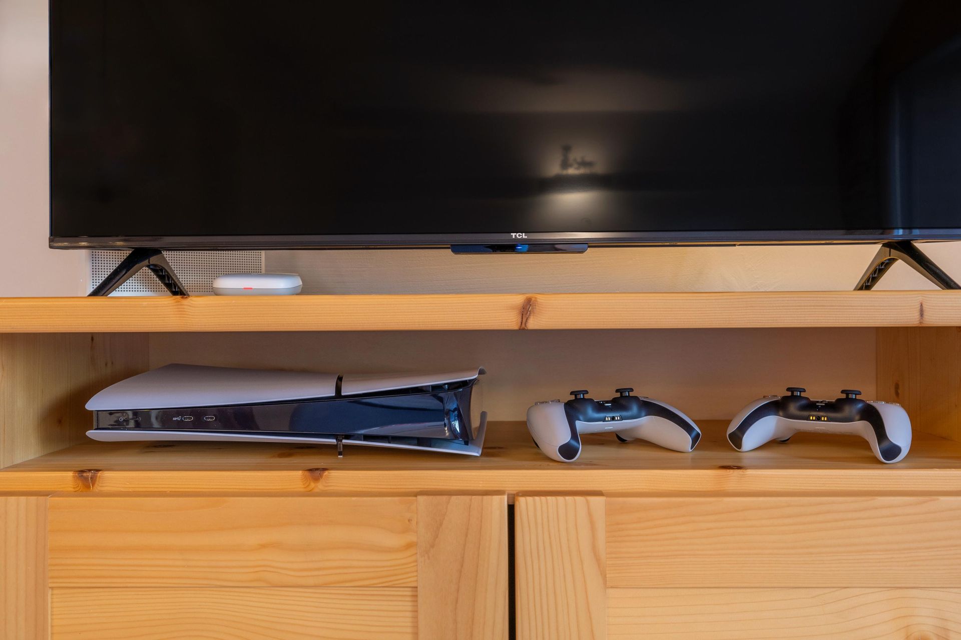 Une console ps5 est posée sur une étagère en bois à côté d'un téléviseur.