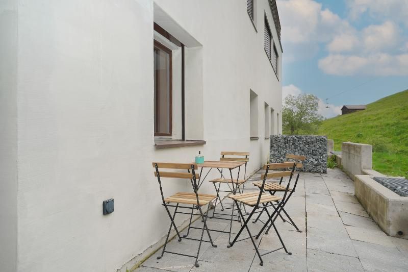 Un patio avec une table et des chaises devant un bâtiment blanc.