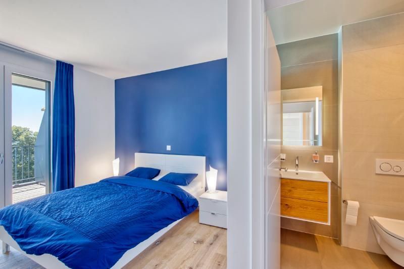 Une chambre avec un lit bleu et une salle de bain avec WC et lavabo.