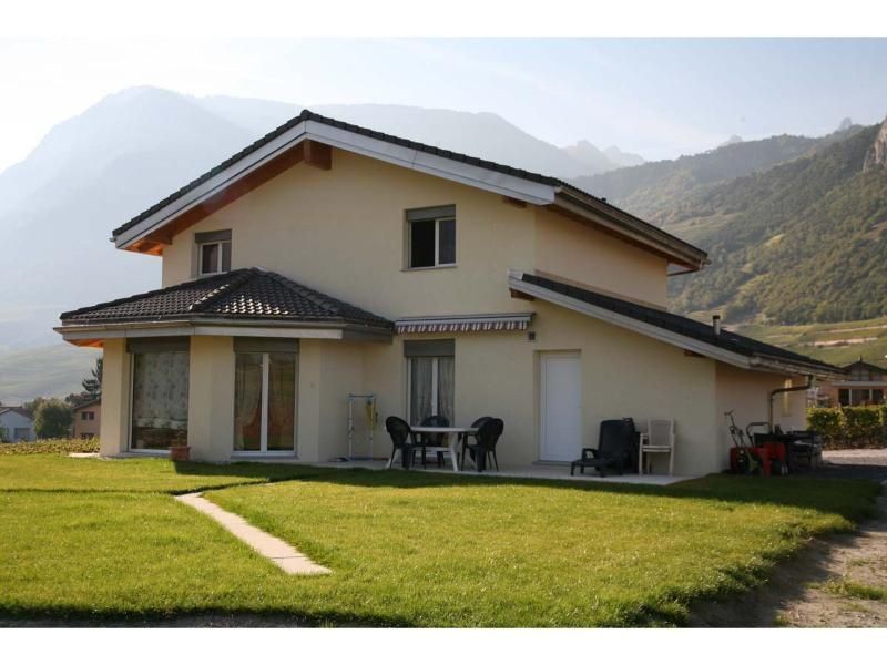 Une maison avec une pelouse devant et des montagnes en arrière-plan