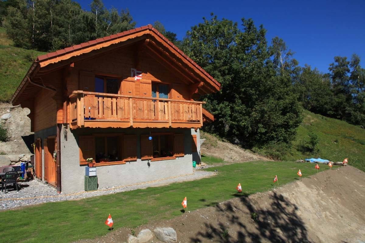 Une maison en bois avec un balcon est assise au sommet d'une colline herbeuse.