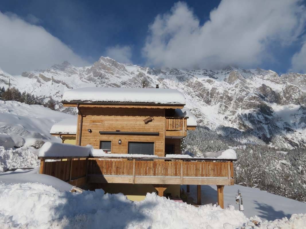 Une maison en bois est entourée de neige et de montagnes en arrière-plan.