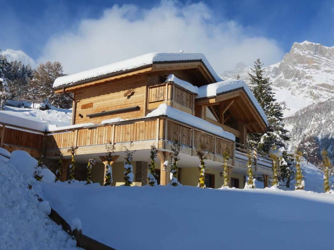 Une grande maison en bois recouverte de neige avec une montagne en arrière-plan.