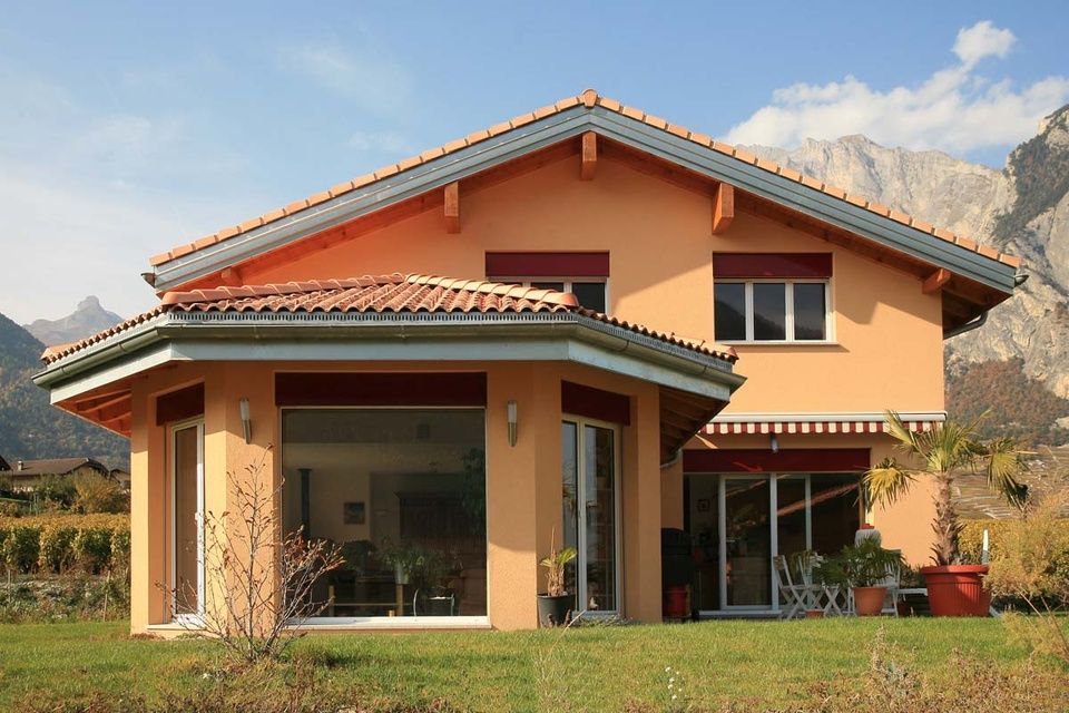 Une maison avec des montagnes en arrière-plan et beaucoup de fenêtres