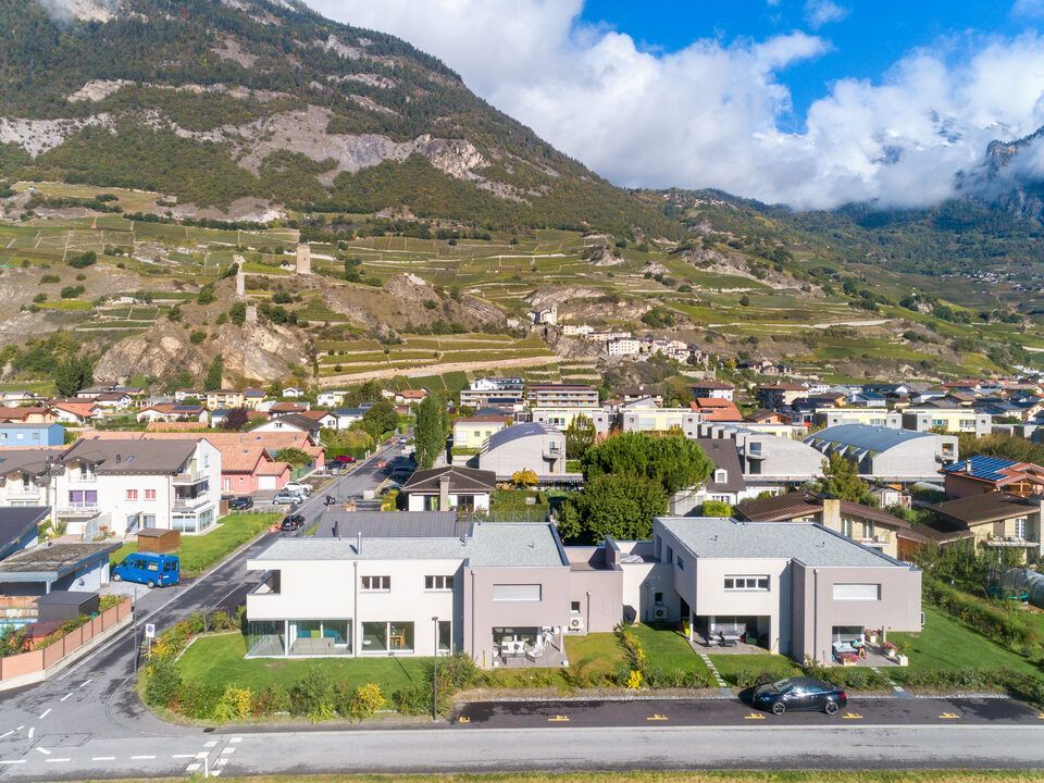 Maisons modernes dans une ville suisse, avec les montagnes en arrière-plan, sous un ciel bleu.