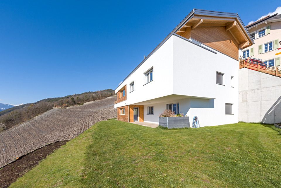 Une maison blanche avec un toit en bois est située au sommet d'une colline verdoyante.