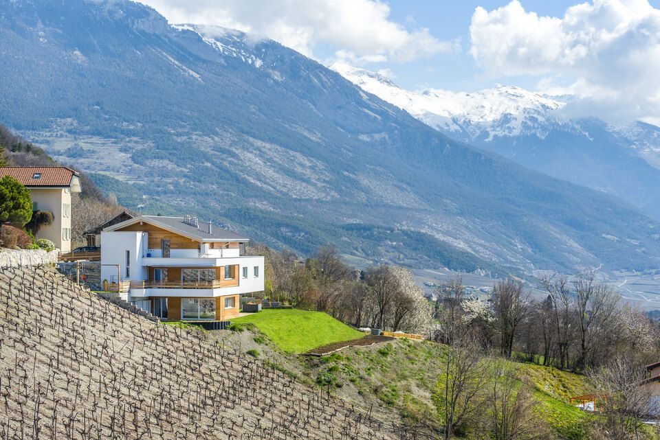 Une maison est assise au sommet d'une colline avec des montagnes en arrière-plan.