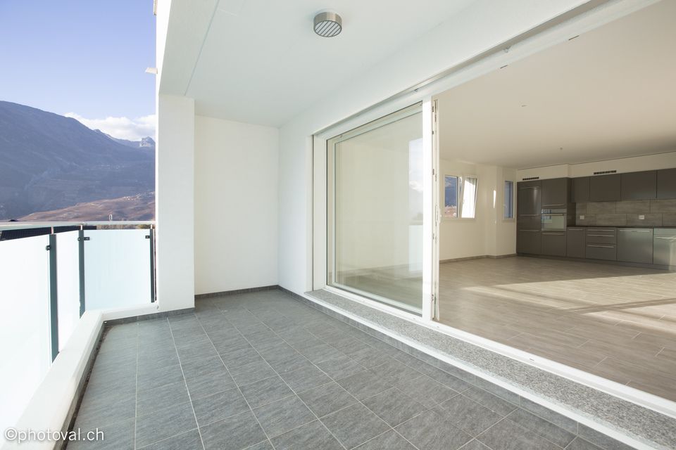 Un balcon vide avec une porte coulissante en verre et des montagnes en arrière-plan