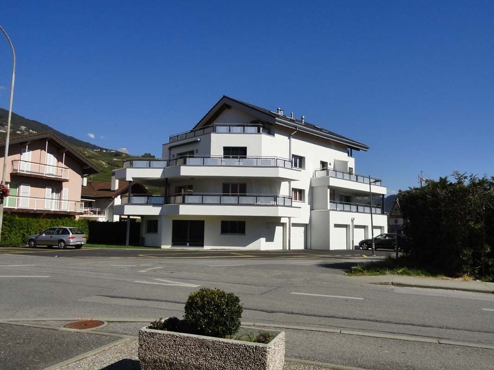 Un grand bâtiment blanc avec des balcons se trouve au coin d'une rue.