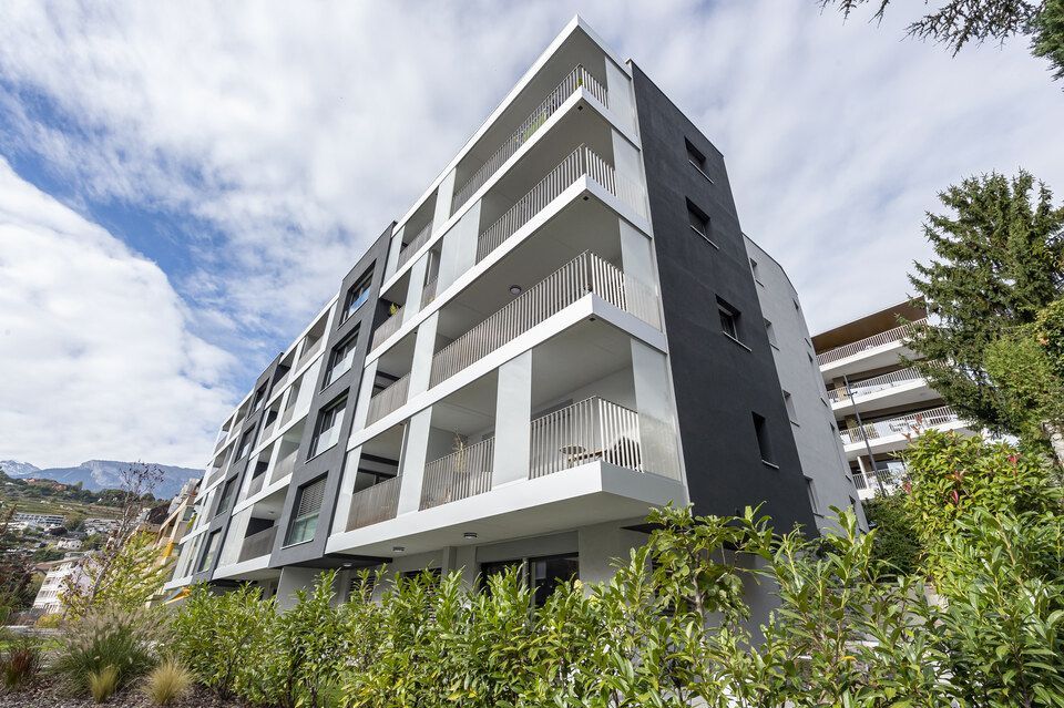 Un grand immeuble d'appartements avec beaucoup de balcons et d'arbres devant lui.