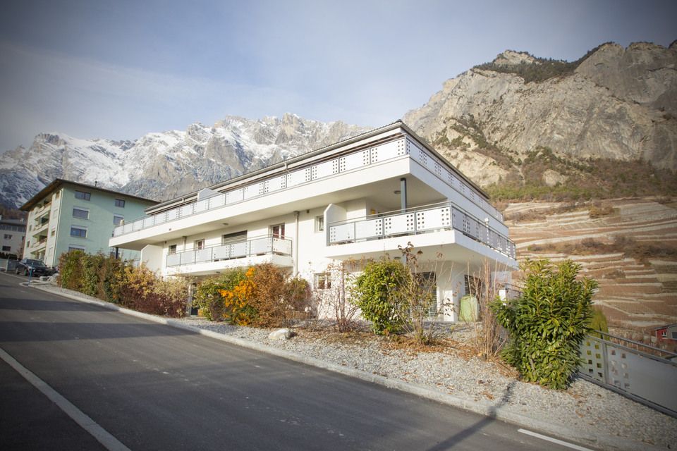 Un grand bâtiment blanc se trouve sur le bord d'une route avec des montagnes en arrière-plan.