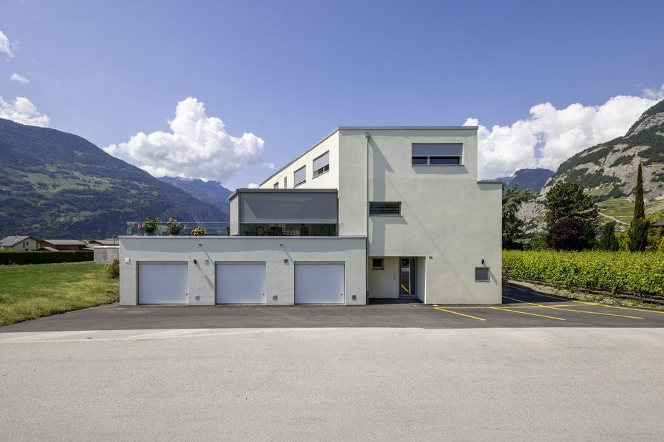 Une grande maison blanche avec trois garages et des montagnes en arrière-plan.