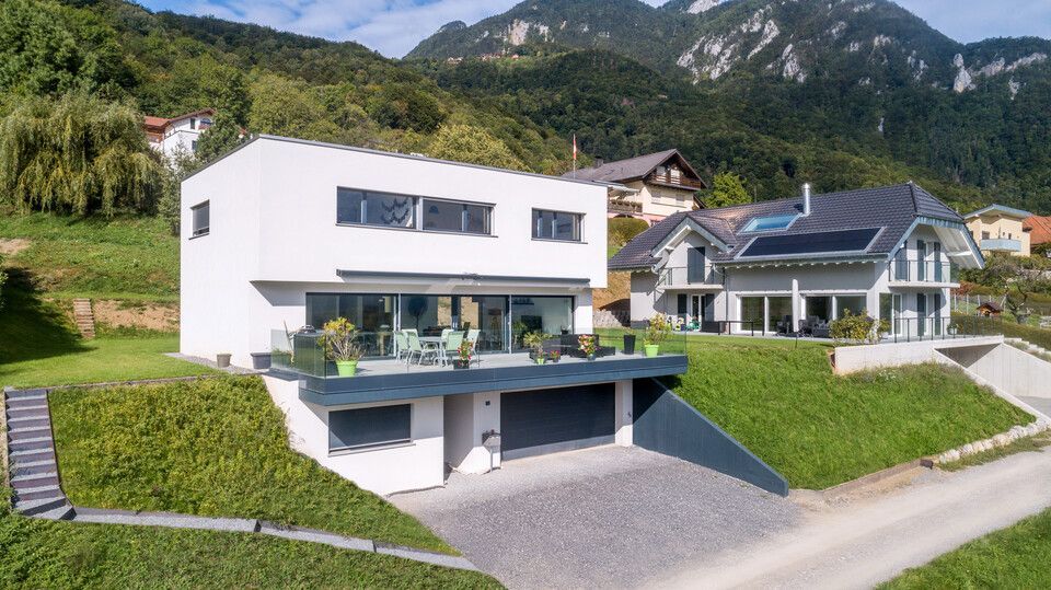 Une maison moderne  au sommet d'une colline avec des montagnes en arrière-plan.
