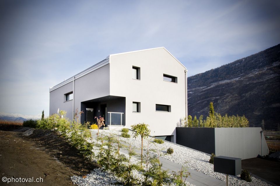 Une maison blanche est assise au sommet d'une colline avec des montagnes en arrière-plan.
