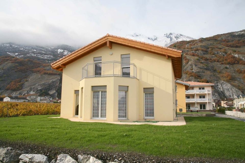Une maison jaune avec un balcon et des montagnes en arrière-plan