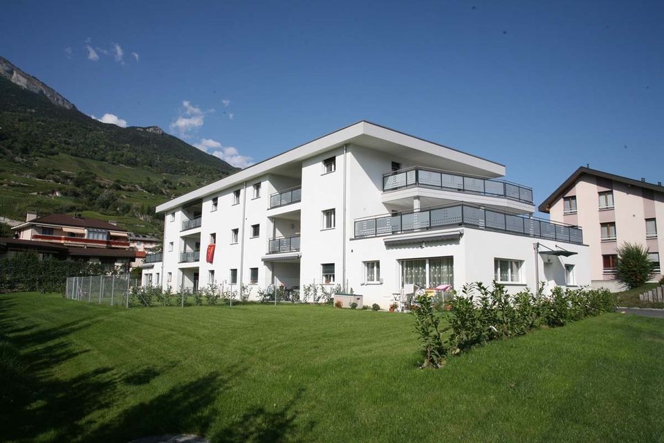 Un grand bâtiment blanc avec des balcons est entouré d'un champ vert luxuriant.