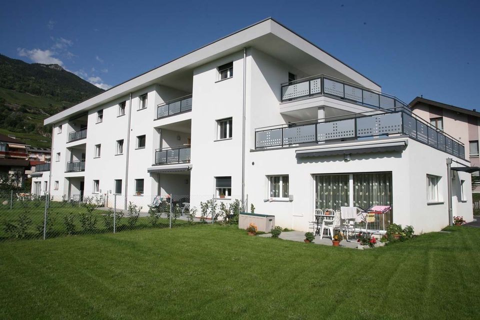 Un grand bâtiment blanc avec des balcons et une pelouse verte luxuriante devant lui