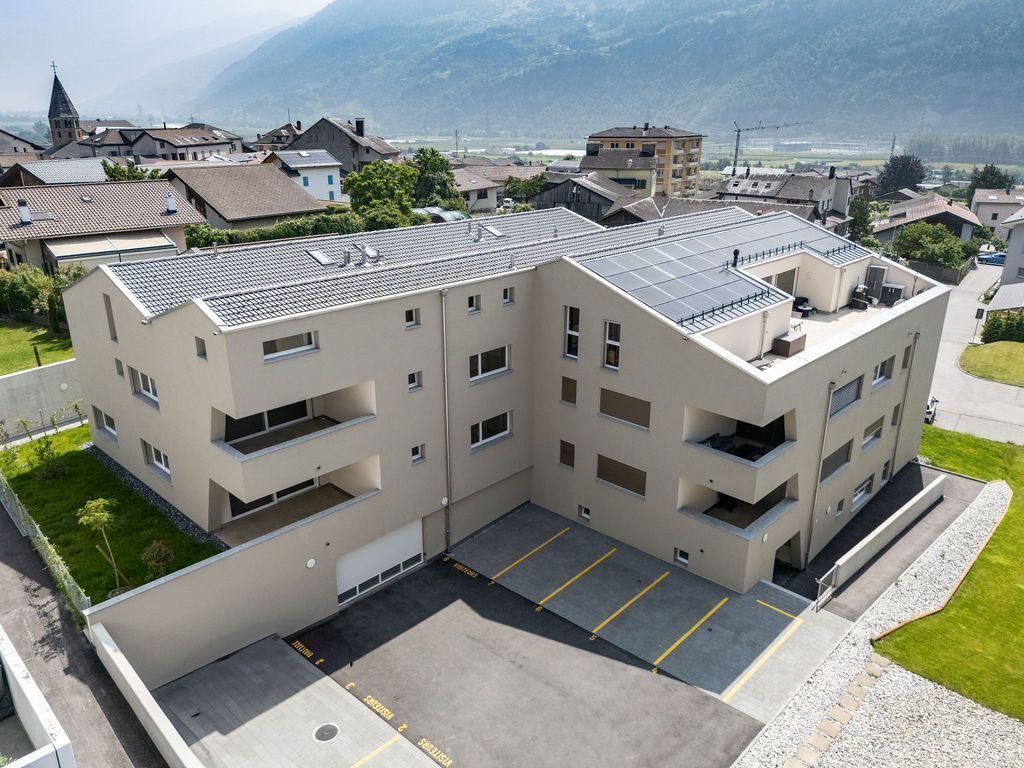 Immeuble d'appartements moderne beige avec parking, situé dans un cadre urbain et montagneux.