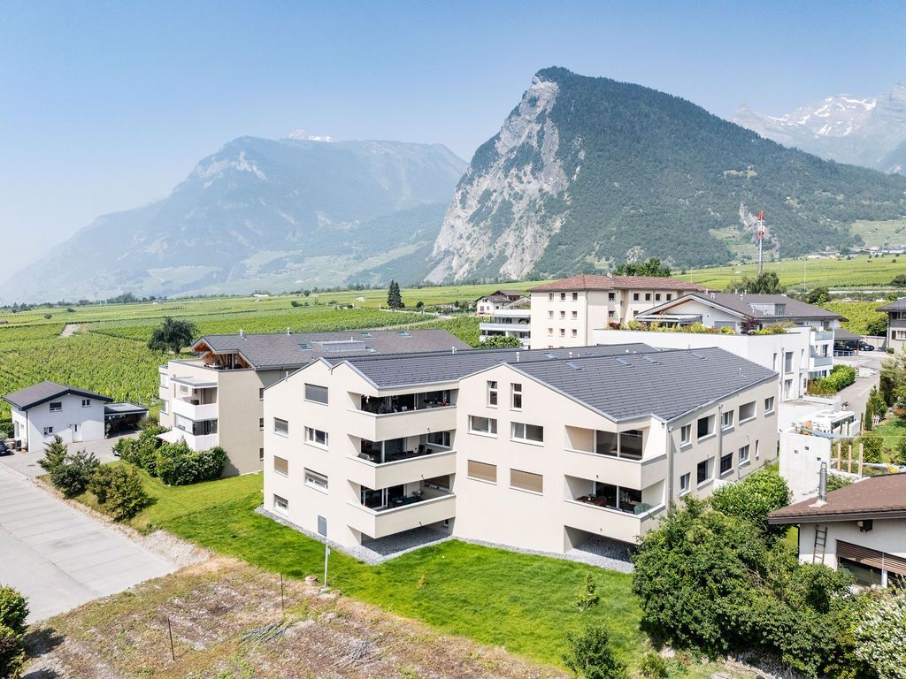 Des immeubles d'appartements nichés sur fond de montagnes et de vignobles, sous un ciel lumineux.