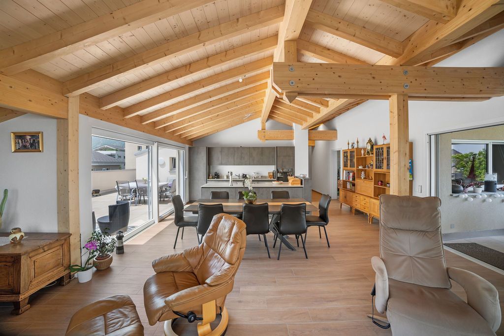 Salon spacieux avec poutres apparentes et cuisine équipée ; comprend un fauteuil inclinable et une table à manger.