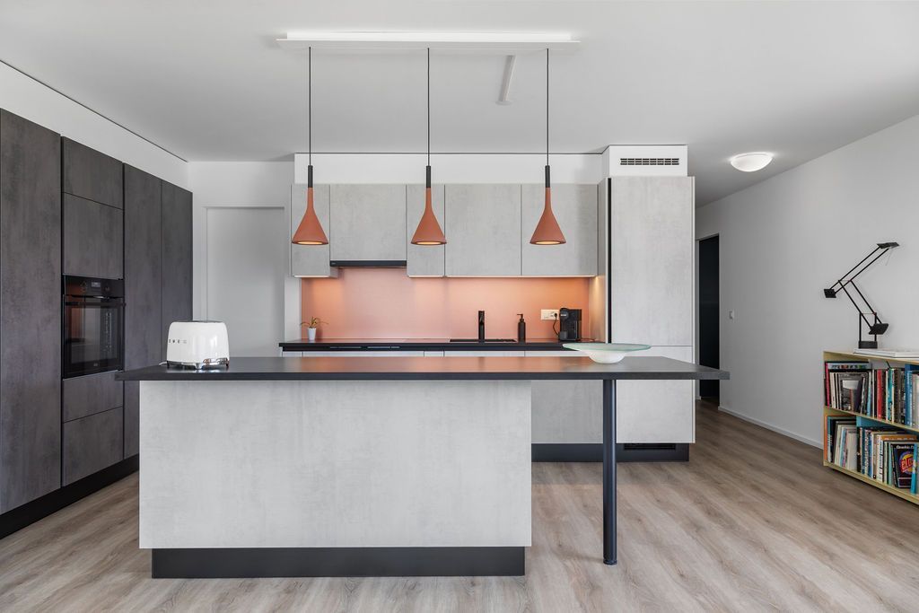 Cuisine moderne avec placards gris, suspensions en cuivre et îlot central avec plan de travail noir.