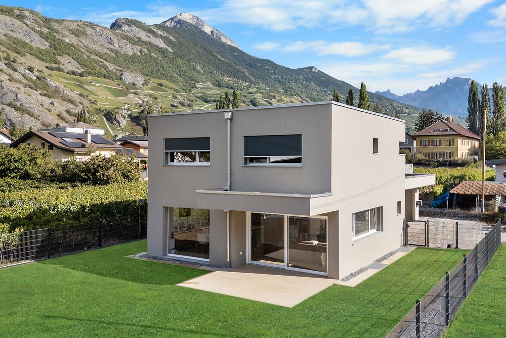 Maison moderne à deux étages avec toit plat, grandes fenêtres et pelouse verdoyante dans un paysage montagneux.
