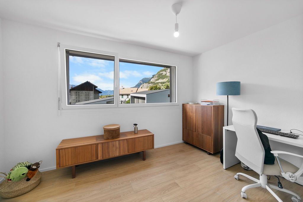 Chambre avec vue sur les bâtiments et les montagnes ; comprend des meubles en bois, un bureau et une chaise de bureau.